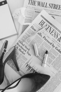 Black and white photo of heels and lipstick laying on top of newspaper