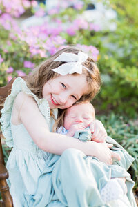 Sister holding her new brother smiling for the camera for her family photographer in Richmond VA