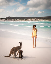 Woman in a yellow swimsuit walking on a beach towards two kangaroos