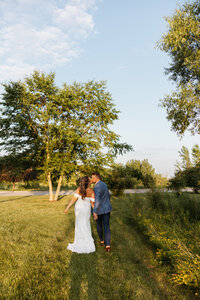 Couple walking through tall grass, candid summer wedding portrait