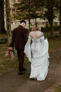Couple holding hands wearing wedding dress and suit holding bouquet.