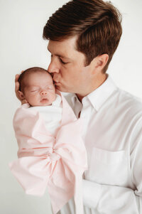 Father kisses his infant daughter during Newborn Photoshoot in Charleston, SC.