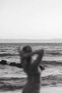Artistic black-and-white photo of a blurred figure standing by the ocean, symbolizing stillness, self-connection, and emotional clarity through nature