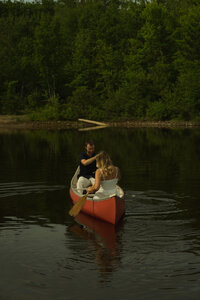 an engaged couple rows toward the camera in a red canoe