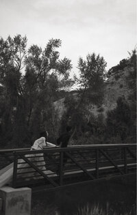 A black and white shot of a soon to be bride and groom running across a bridge.