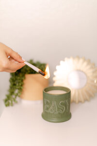 Merlyn Asencio lighting a green candle with a match, surrounded by a plant, symbolizing peace, mindfulness, and the calming atmosphere central to her trauma therapy practice in Miami, Florida