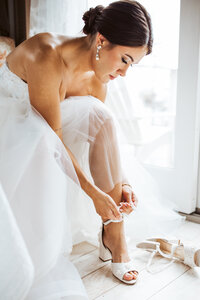 Bride adjusting her shoe while getting ready on the morning of her Maine wedding.