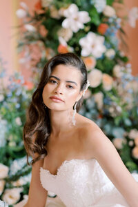 closeup of a bride wearing a corseted wedding dress sitting in front of a floral wall in the ballroom at avington park