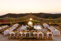 A far away shot of the entire Reception detail and table set ups with string lights from above and long style family tables.