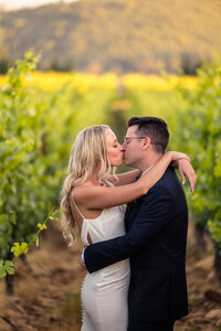 Bride and groom kissing in vineyard.