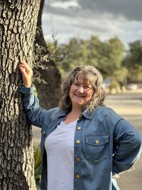 woman with curly blonde hair wearing a jean jacket and smiling