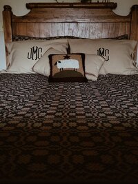 Oak bed headboard with early american textile coverlet and monogrammed flax colored linen pillow cases