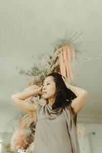 A woman holding her head and looking to the side in front of a large floral installation. 