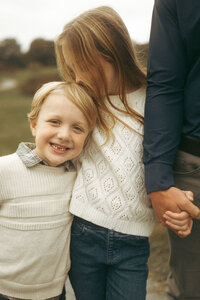 A sister kisses her smiley younger brother on the head.