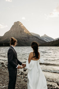 a bride and groom standing a looking at a mountain range with grand views surrounded by water