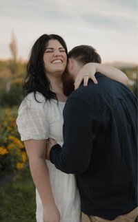 Brigette of Judith Photo Co. smiling while her husband Michael kisses her neck.
