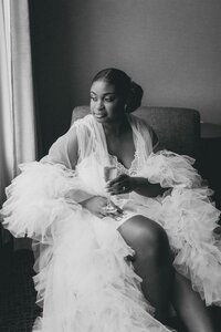 bride sitting in a chair looking out the window while holding a glass of champagne