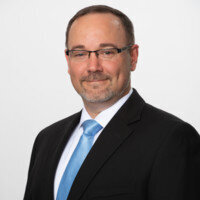 Jason Tomsic, member of Normal 40 in a suit with blue tie for his testimonial image