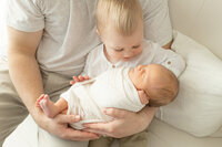 Older sibling holding a newborn baby in their arms, gazing down lovingly.