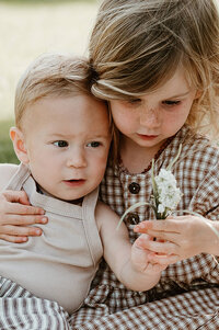 Siblings admiring a flower during a warm Charlotte family photography session outdoors.
