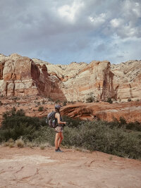 Elopement photographer standing on red rock formations in Page, Arizona, overlooking Horseshoe Bend. She holds a film camera under a clear blue sky, capturing the desert landscape in a candid, adventurous moment.