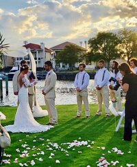 wedding venue pensacola showing February's bride and groom in her white wedding dress and he is in dark gray suit with a boutinaire with white shirt.  Scenic background with water in in the background along with upscale luxury boats and homes along with docking.  