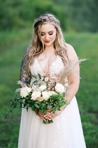 Bride looking at her bouquet at a scenic Minnesota farm with green grass | Toly Dzyuba Photography | Minnesota wedding photographer