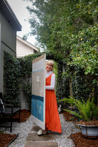 Adele walking in overgrown garden carrying large abstract painting
