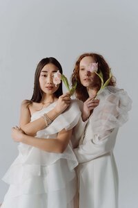 two women in white holding one pink flower to their eyes