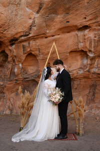 Bride and Groom eloping in Arches National Park in a wedding dress and black suit with a wedding arch.