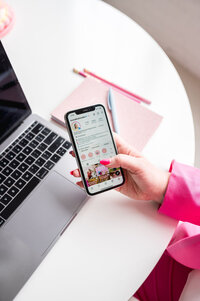 Kat's hand holding an iphone in front of her laptop on a table