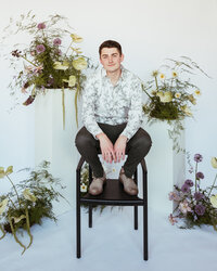 Cole Buys seated with floral background.