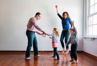 Gina and her family dancing and holding hands in a circle, with a window letting in natural light.