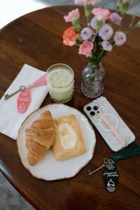 Branded breakfast setup with croissant, pastry, flowers, and Sugarpunch Marketing® key tag, on a coffee table.