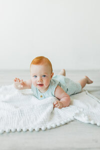 Portland Newborn Photographer_ baby milestone photos showing a red head baby boy lying on his tummy smiling at the camera in studi 