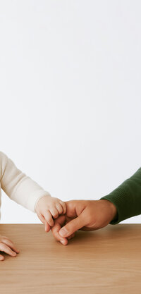 A toddler child's hand and a grown man's hand holding one another lovingly, to represent paternity mediation.
