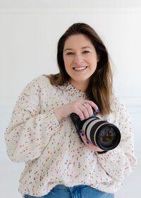 Wedding and senior photographer in Twin Cities, holding her camera and wearing jeans with a white top in front of a white background