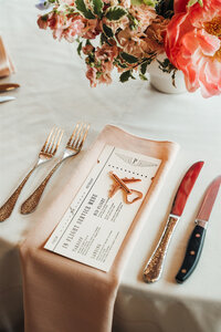Wedding menu with airplane details sitting on a napkin featuring a bottle opener and calligraphy details representing full service design and calligraphy by Life in Letters.