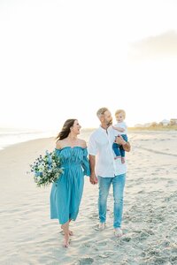 family walking on beach with toddler baby boy and flower bouquet