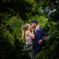 Couple sharing a kiss inside a heart naturally formed by trees, showcasing award-winning wedding photography.