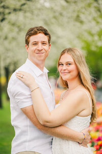 A man and his fiance stand embracing and looking at the camera in the blooming Keukenhof garden in Lisse