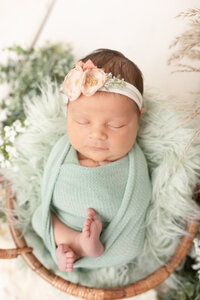 newborn baby girl wrapped in mint with greenery and florals