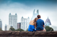 Couple sitting on a wall while the girl lays her head on the boys shoulder overlooking the Atlanta skyline at Piedmont Park