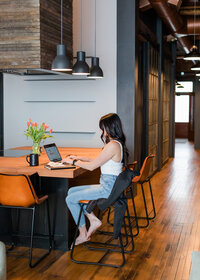 Allie Clark working on a MacBook at a modern wood-and-black table setup, reflecting the creative process behind Allie Clark Designs.