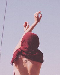 Woman in headscarf raising arms in joy against pink sky on soulful retreat
