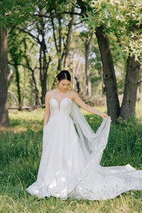 A bride in a spaghetti strap gown with a deep v swishes her veil back and forth while standing in a forest. Photo by Anna Brace, a wedding photographer in Omaha, Nebraska.