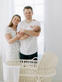 parents holding newborn baby in front of bassinet