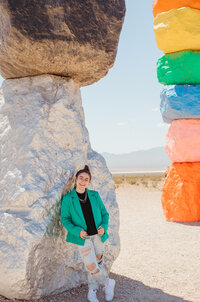 Girl in a green blazer smiling in front of a silver rock.