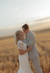 A groom gently holds the neck of his bride as he is about to kiss her. They're standing in a wheat field near Idaho Falls, Idaho.