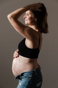 une jeune femme enceinte de profil qui pose au soleil pendant un shooting grossesse avec la photographe studio sensigraphie à la tour du pin en Isère